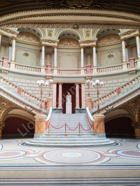 Symmetrical marble staircase with gilded details, pink columns, and a central statue.
