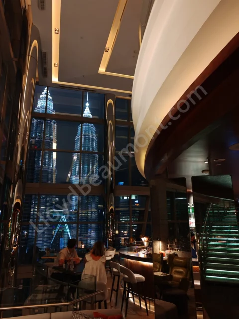 Evening lounge with a sweeping staircase and illuminated twin towers visible through tall windows.