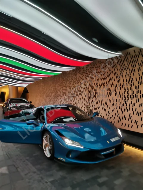 Blue Ferrari with its door open beneath a brightly illuminated entrance canopy.