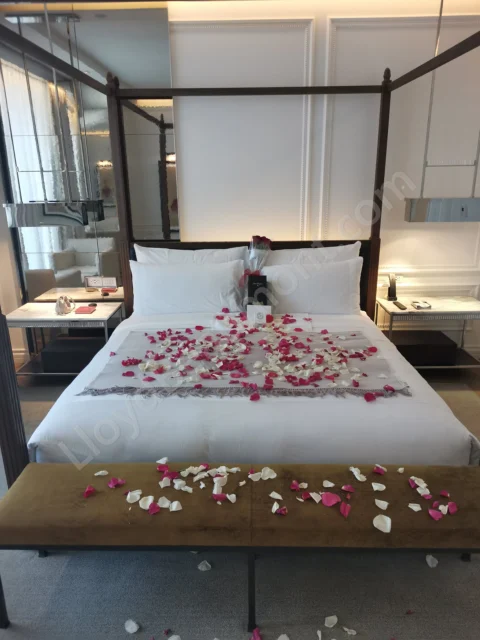 Four-poster bed scattered with rose petals, with roses and champagne arranged against white pillows.