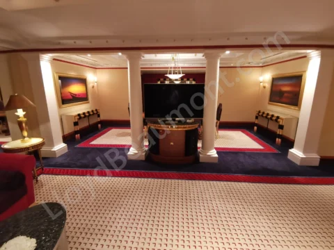 Grand hotel suite sitting area with white columns, a central television, and patterned red-and-blue carpeting.