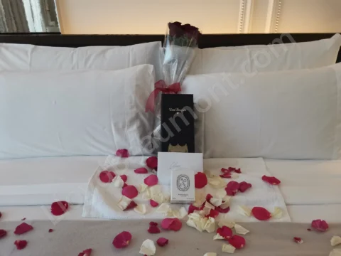 Roses, champagne, and a candle surrounded by red and white petals on a hotel bed.