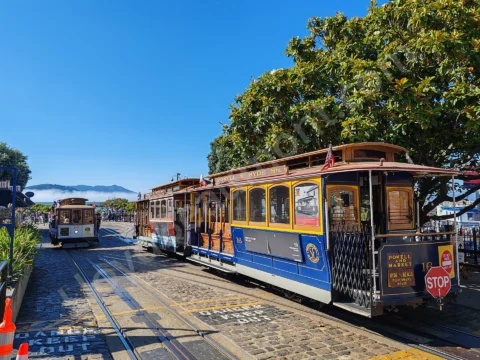 Classic San Francisco cable cars waiting on tracks beneath a bright blue sky.