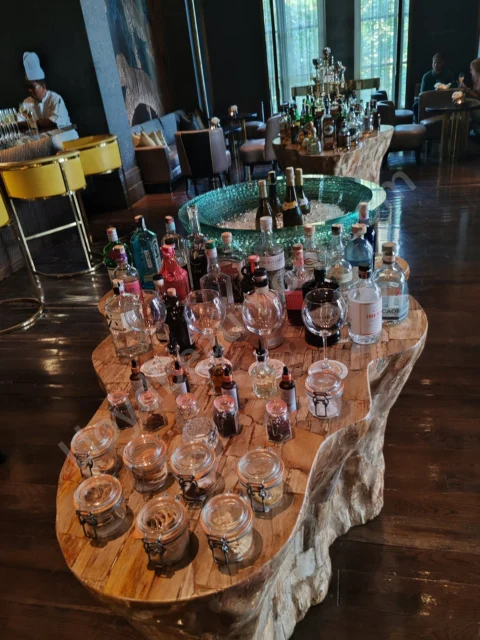 Spirits and botanical ingredients displayed on sculptural wooden tables in a hotel lounge.