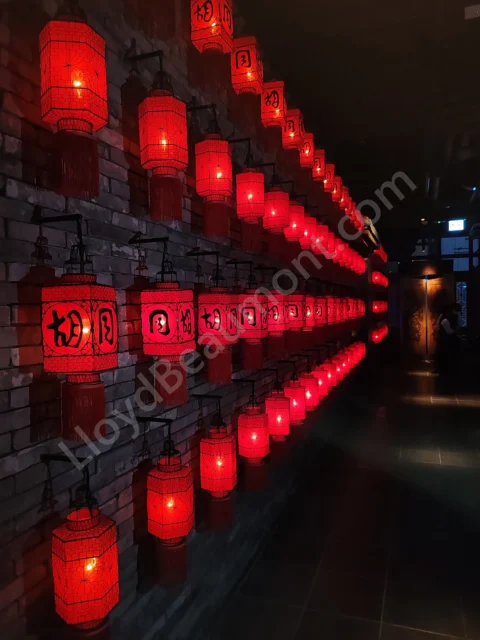 Rows of glowing red lanterns along a dark brick-lined restaurant corridor.