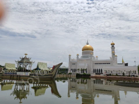 White mosque with a golden dome reflected in still water beside an ornate ceremonial boat.