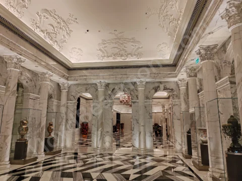 Marble hotel gallery with classical columns, decorative vases, and a geometric black-and-white floor.