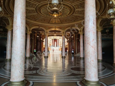Grand columned foyer with patterned stone floors, ornate ceilings, and a staircase beyond.