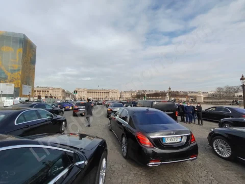 Black luxury cars gathered in a broad historic city square.