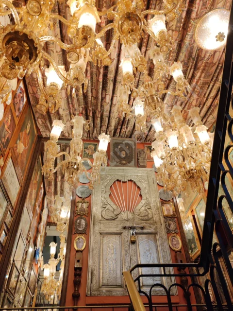 Dense clusters of golden chandeliers illuminate an elaborately decorated interior staircase.