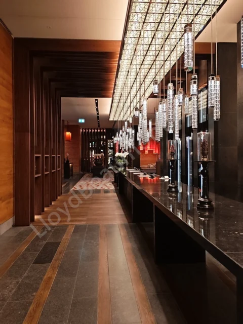 Warm wood hotel corridor lined with glass pendant lights and a polished dark counter.